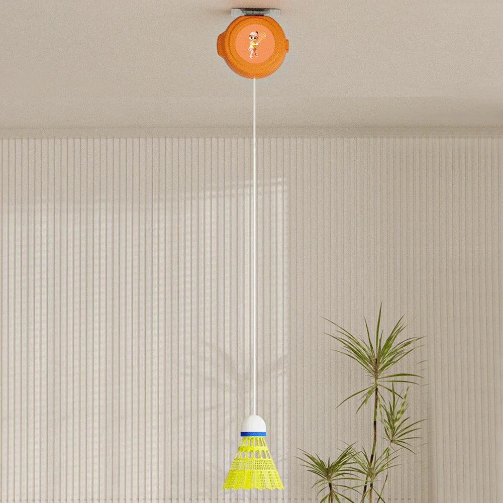 Badminton training equipment suspended from the ceiling with an orange rebound device and a yellow shuttlecock in a minimalist white room with a potted plant.