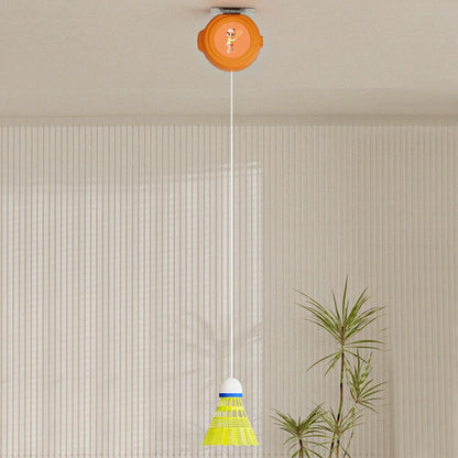 Badminton training equipment suspended from the ceiling with an orange rebound device and a yellow shuttlecock in a minimalist white room with a potted plant.