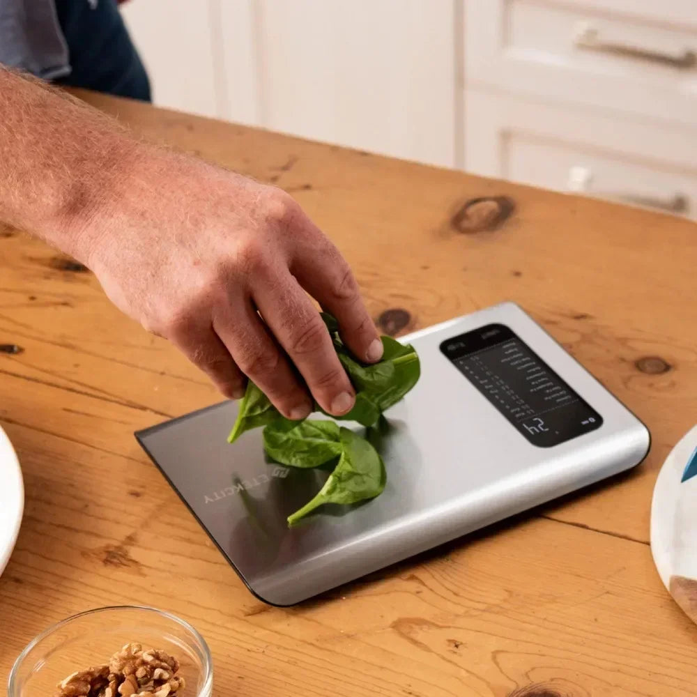 Precise kitchen scale weighing spinach leaves on wooden counter