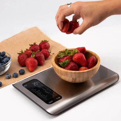 Digital food scale with fresh strawberries, blueberries, and a hand placing a strawberry on the scale for accurate measurement in ounces, grams, or milliliters.