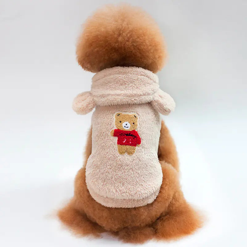 Furry, tan-colored pet coat with teddy bear design and bear ear hood, resting on white background